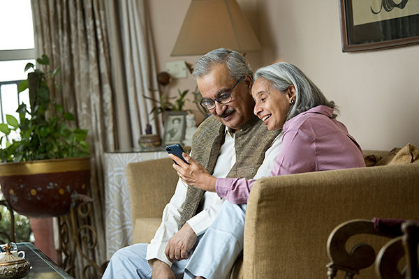Una pareja de ancianos en un sofá mirando un teléfono inteligente
