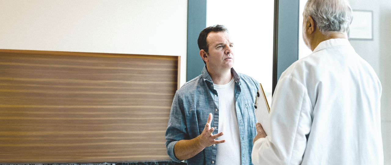 Resigned looking middle-aged man discussing findings with doctor holding a clipboard